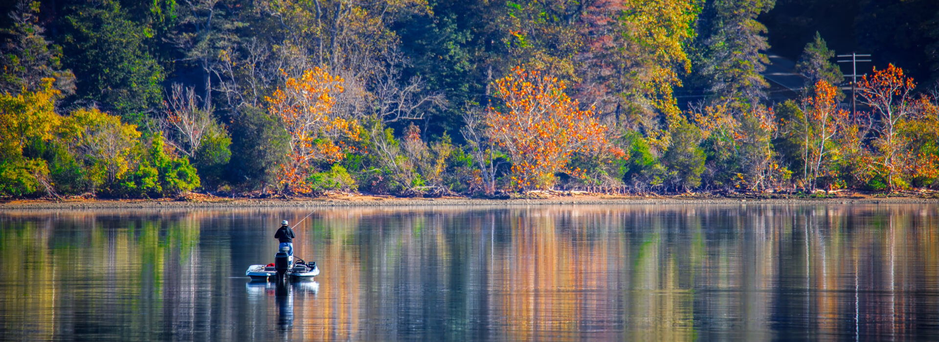 A man fishing by himself on a Virginia waterway with an autumn forest in the background.
